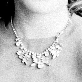 Woman in a necklace sits before a patterned wall.