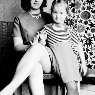 Woman and child standing near patterned wallpaper.