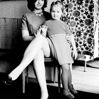 Woman and child standing near patterned wallpaper.