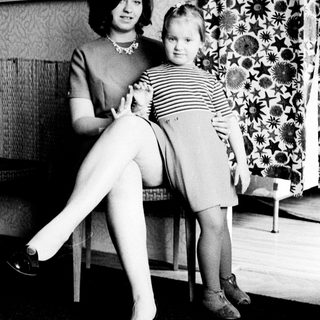 Woman and child standing near patterned wallpaper.