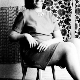Woman sits in chair, posing in a black and white photograph.