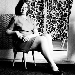 Woman sits in chair, posing in a black and white photograph.