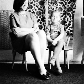 Woman and child seated, smiling, in a vintage interior.