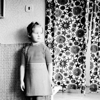 Black and white photo of a young girl standing indoors.