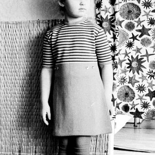 Black and white photo of a young girl standing indoors.