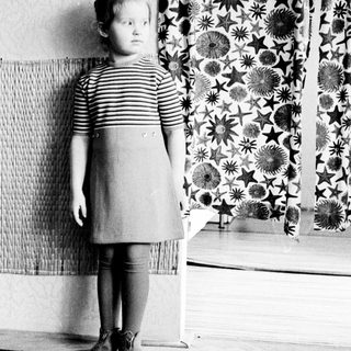 Black and white photo of a young girl standing indoors.