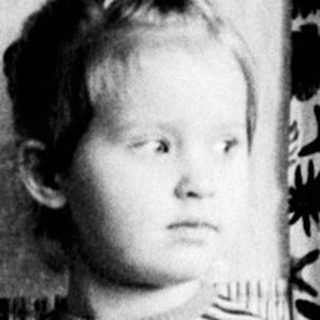 Black and white photo of a young girl standing indoors.