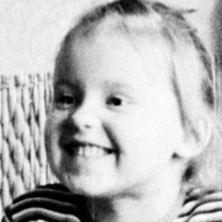 A young girl sits smiling, facing away from the camera.