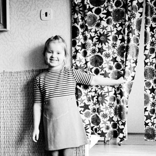 Young girl stands near a curtain in a room.