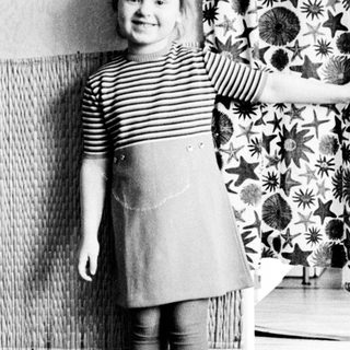 Young girl stands near a curtain in a room.