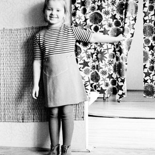 Young girl stands near a curtain in a room.