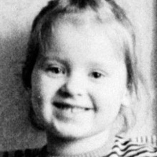 Young girl stands near a curtain in a room.