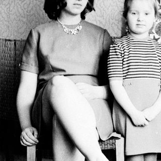 Woman and child stand in a room, looking apprehensive.