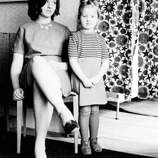 Woman and child stand in a room, looking apprehensive.