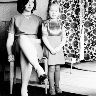 Woman and child stand in a room, looking apprehensive.