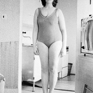 Woman in a swimsuit stands in a vintage bathroom.