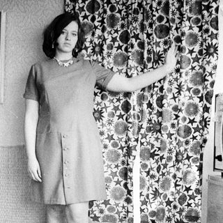 Woman in a dress stands with arm raised, indoors.