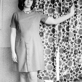 Woman in a dress stands with arm raised, indoors.