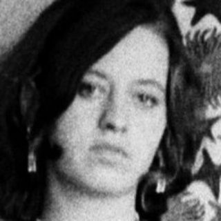 Woman in a dress stands with arm raised, indoors.