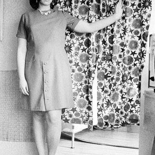 Woman in a dress stands with arm raised, indoors.
