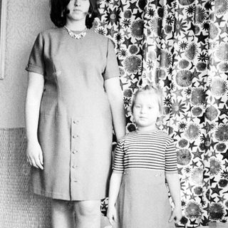 Woman and child stand in front of patterned curtain.
