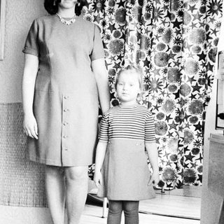 Woman and child stand in front of patterned curtain.