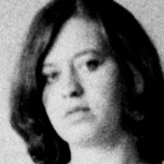 Woman in leotard poses near a door and table.