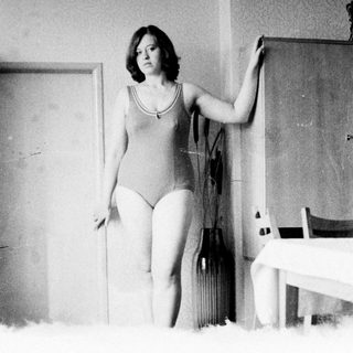 Woman in leotard poses near a door and table.