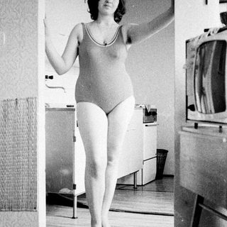 Woman in swimsuit standing in a vintage bathroom.