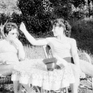 Two people sit on chairs outdoors in a grassy area.