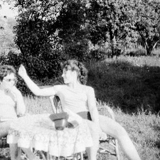 Two people sit on chairs outdoors in a grassy area.