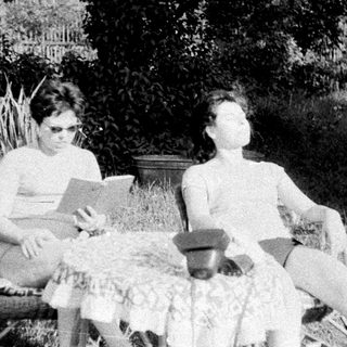 Two people relax outdoors, one reading, in a grassy area.