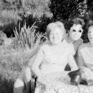 Two women seated in tall grass, outdoors.