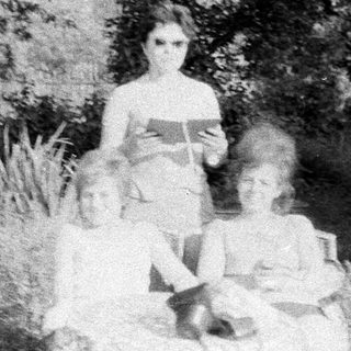 Woman with two children seated in grassy, wooded area.