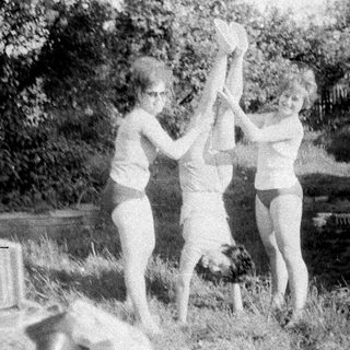 Three girls playfully suspended upside down in a yard.