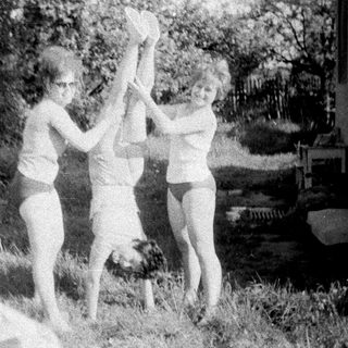 Three girls playfully suspended upside down in a yard.