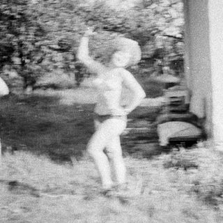 Here's a brief summary of the image: Child playfully jumping outdoors near a building.