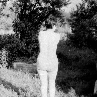 Two nude figures standing in tall grass and foliage.