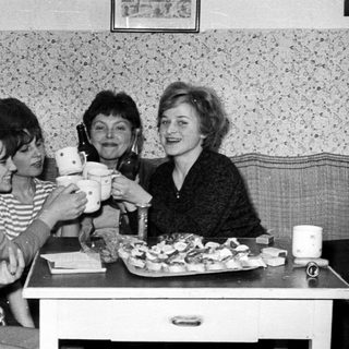 Four women toasting with teacups at a table.