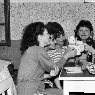 Four women toasting with teacups at a table.