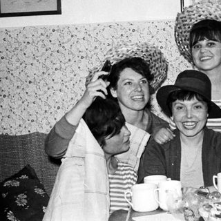Group of women playfully wearing hats and smiling.