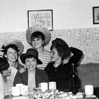 Group of women playfully wearing hats and smiling.
