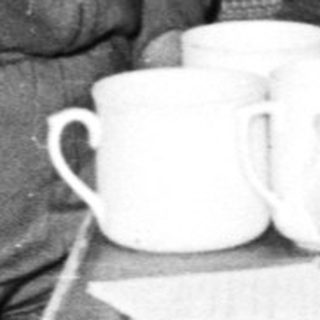 Here's a brief summary of the image: Women seated indoors, enjoying refreshments, wearing hats.
