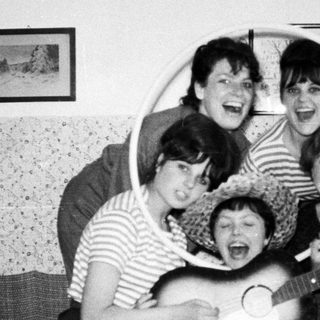 Group of women playing instruments and laughing indoors.
