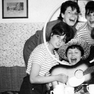 Group of women playing instruments and laughing indoors.