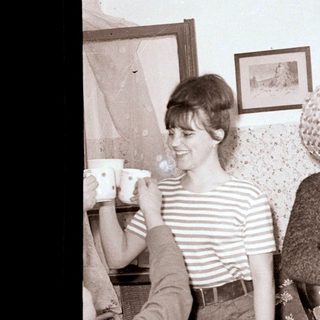 Here's a brief summary of the image: A young woman smiles while someone raises a teacup.
