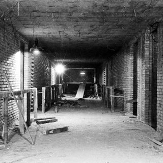 Here's a brief summary of the image: Unfinished brick corridor with temporary supports and debris.