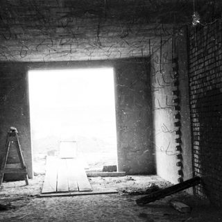 Here's a brief summary of the image: Abandoned, unfinished brick room with a bright doorway.