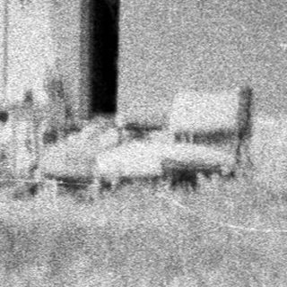 Here's a brief summary of the image: Old house with overgrown grass and a person on the porch.