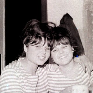 Two smiling women embrace in a vintage black and white photo.